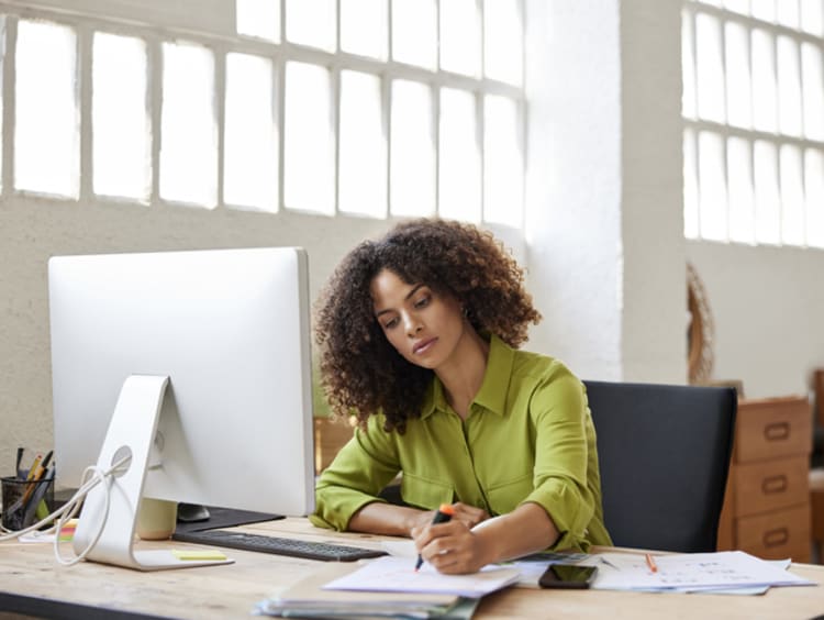 Woman writing at her desk with a notebook in an office