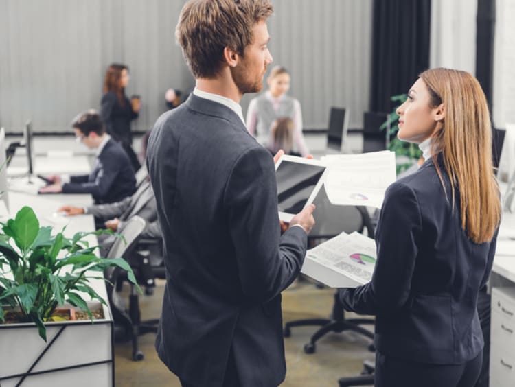 Business woman and man talking in a busy office setting 