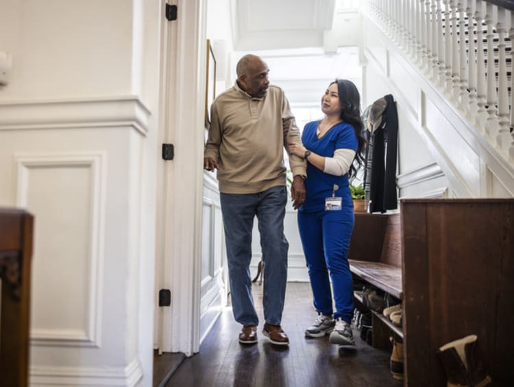 Female nurse aiding a senior man with walking at home