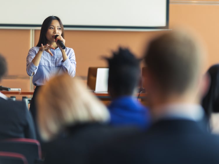 woman speaking into a microphone in front of a crowd