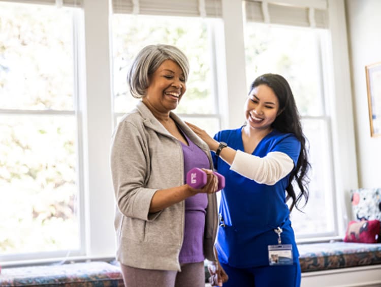 At home nurse helping senior woman with physical therapy at home.