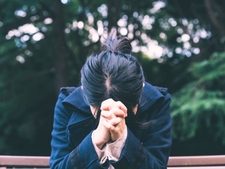 Women bowing her head in prayer on a bench outside