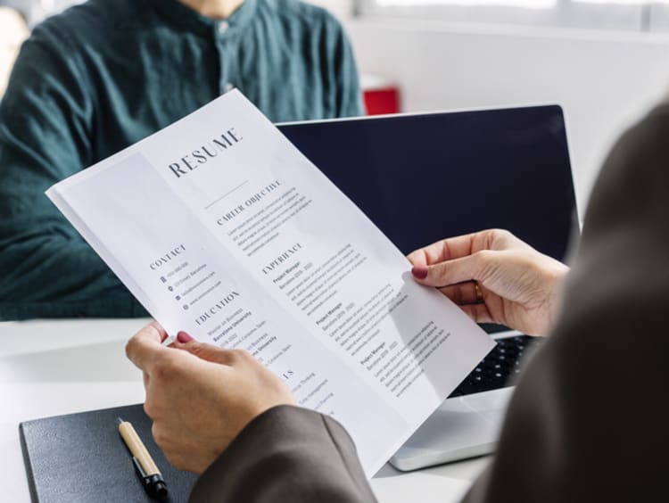 Hands of recruiter holding resume in front of candidate at desk - stock photo