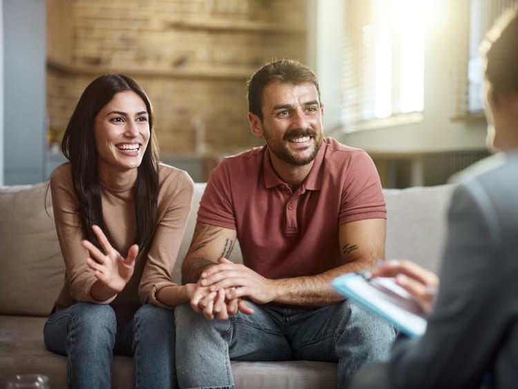 Couple smiling on a couch opposite a counselor