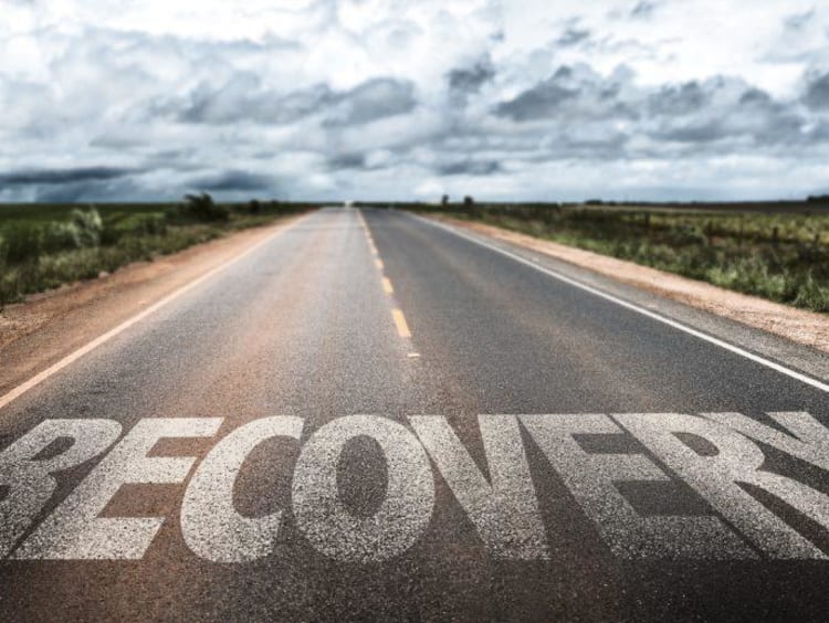 Large letters spell recovery on empty road with a cloudy sky ahead