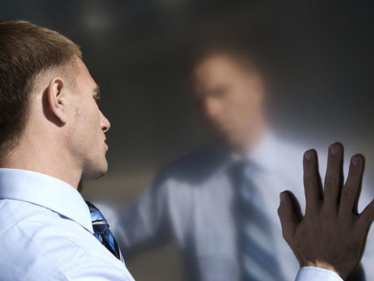 A man looking at his reflection with hands touching the mirror