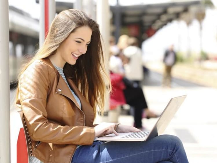 Young brunette woman smiles while using laptop at light rail station