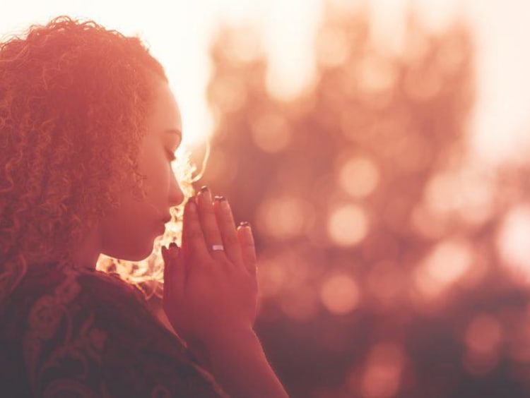 Young woman praying in view of a sunset