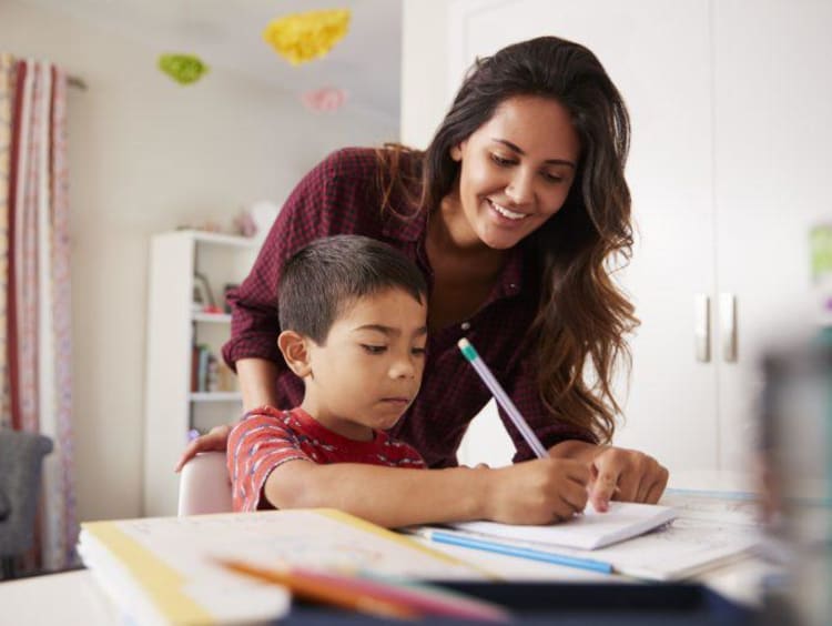 Mom stands behind boy doing his homework