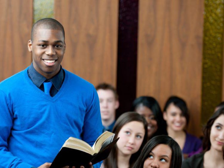 Young male pastor holds bible in full classroom