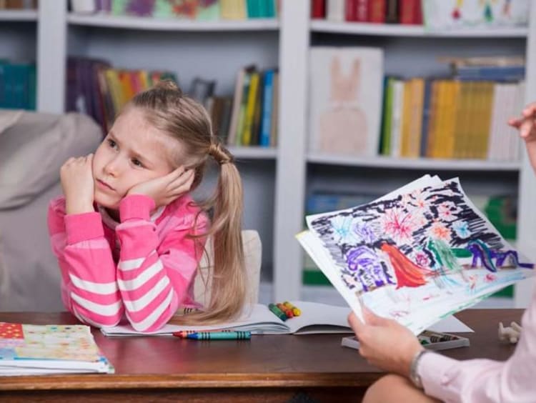 Professional child counselor looks at little girl's drawing while girl in pink looks distressed