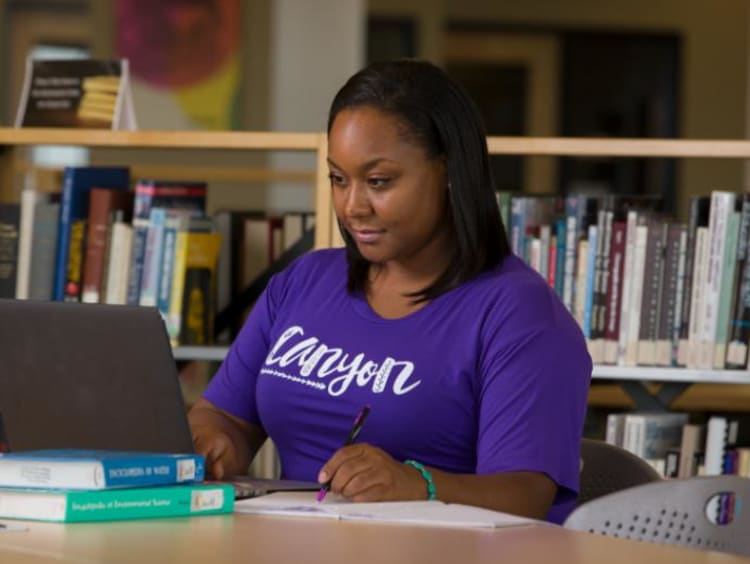 GCU Student in library working on laptop