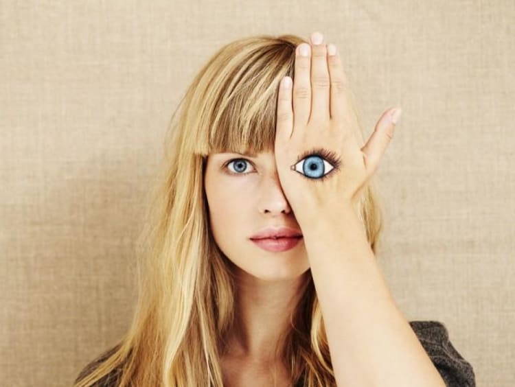 Woman covering her left eye with a painting of an eye on her hand