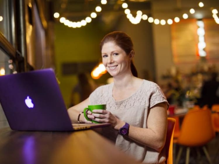 Girl smiles while using her laptop in a trendy coffeeshop