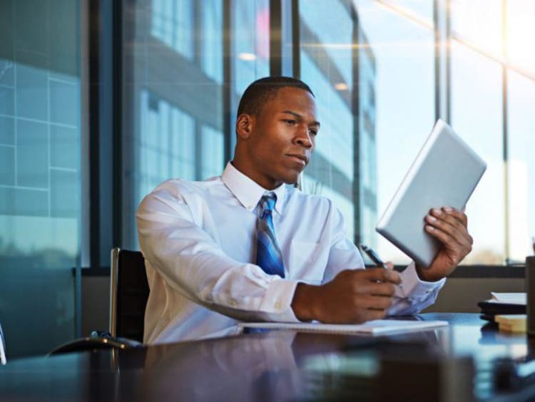 African american businessman reads technical article on tablet and takes notes