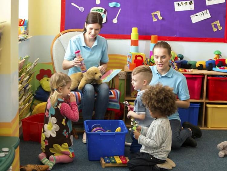 Two nursery workers play with kids in colorful nursery