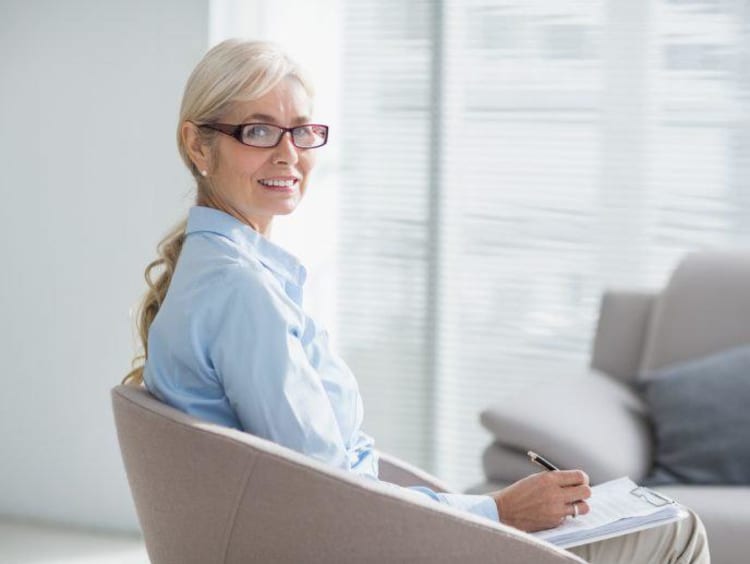 Cognitive psychologist turns around in chair with glass window showing high rise view outdoors