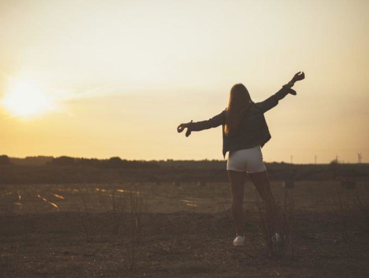 girl standing in a field at sunset with her arms out
