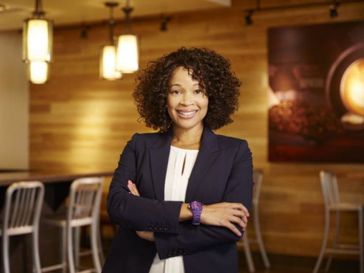 Doctoral student stands with arms crossed in a modern cafe