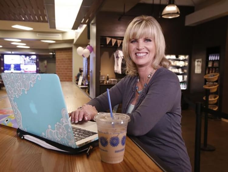 Middle-aged blonde sits a high rise table in a coffee shop