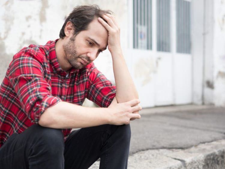 Young male looks depressed sitting at the curb