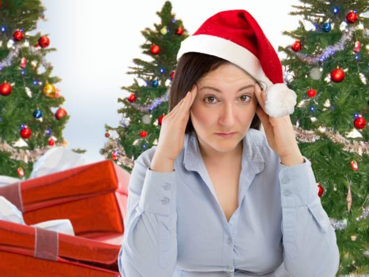 A woman in a Santa hat rubbing her temples in front of a Christmas tree