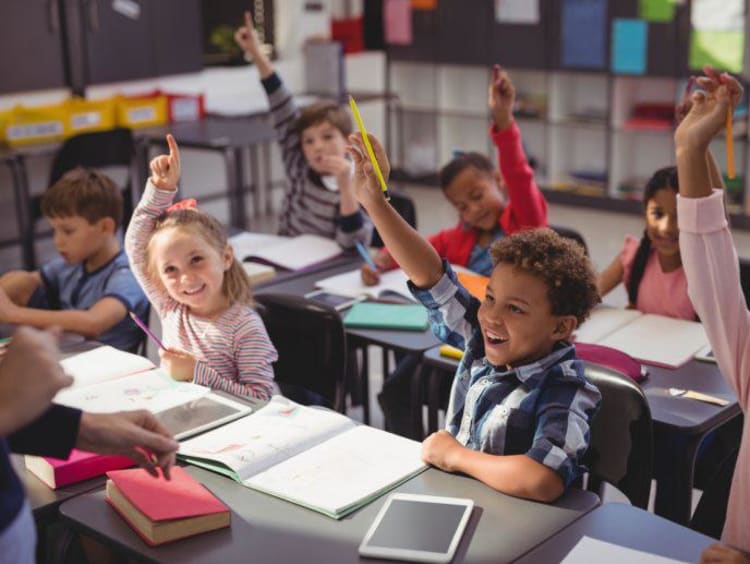 Children raise hands to answer a question in classroom setting