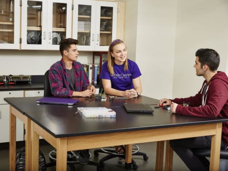 three students sitting at a desk and talking