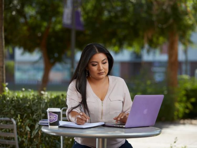 Doctoral student takes notes from laptop outdoors at GCU campus