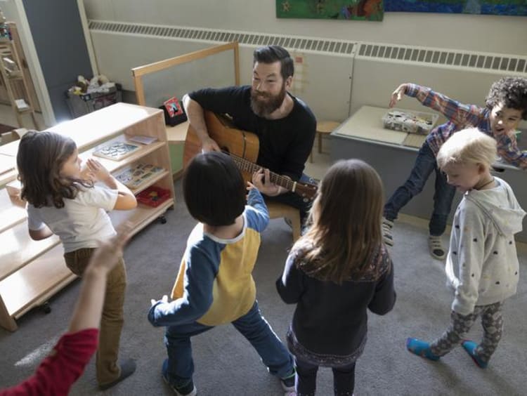 Man playing guitar with little kids around him