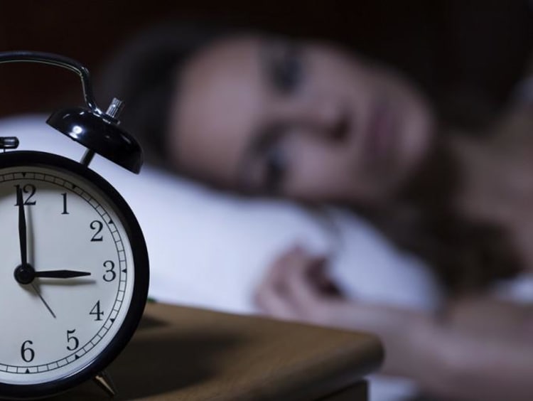 woman laying in bed looking at alarm clock