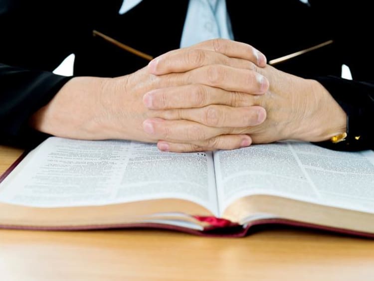 A pair of hands folded over the Bible