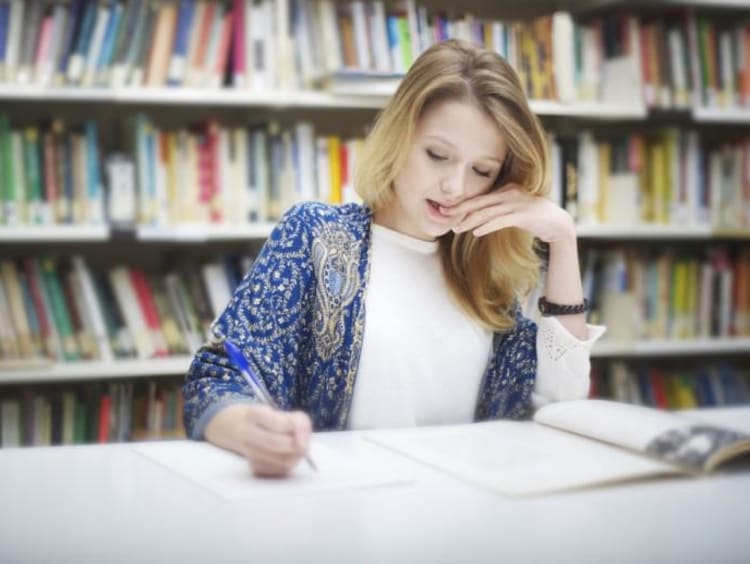 Blonde female student bites nails while studying in library