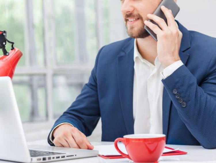 Adult man talks on cellphone sitting at a counter with a laptop 