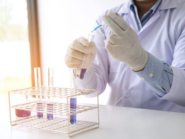 Male scientist puts blue liquid in test tube with red liquid in it