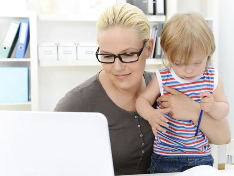 mom holding child and working on the computer