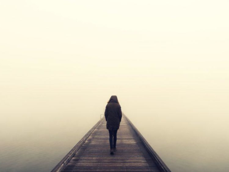 A man walking alone on a foggy bridge