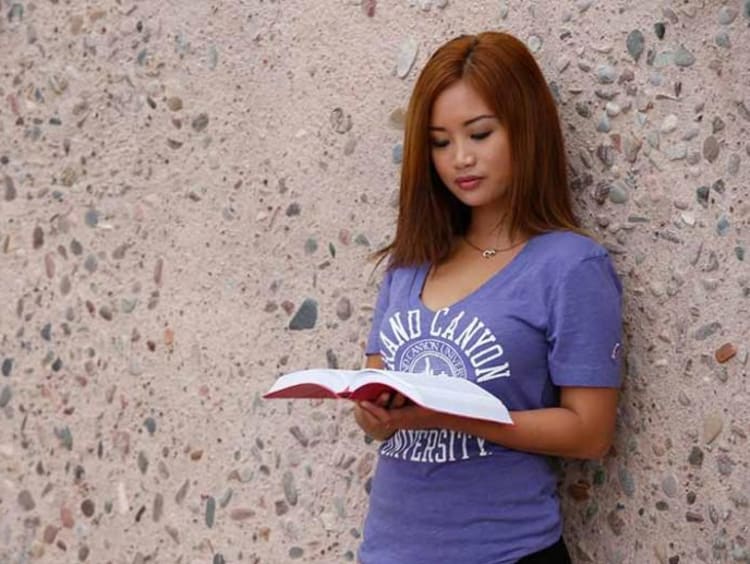 Woman reading a book against a stone wall