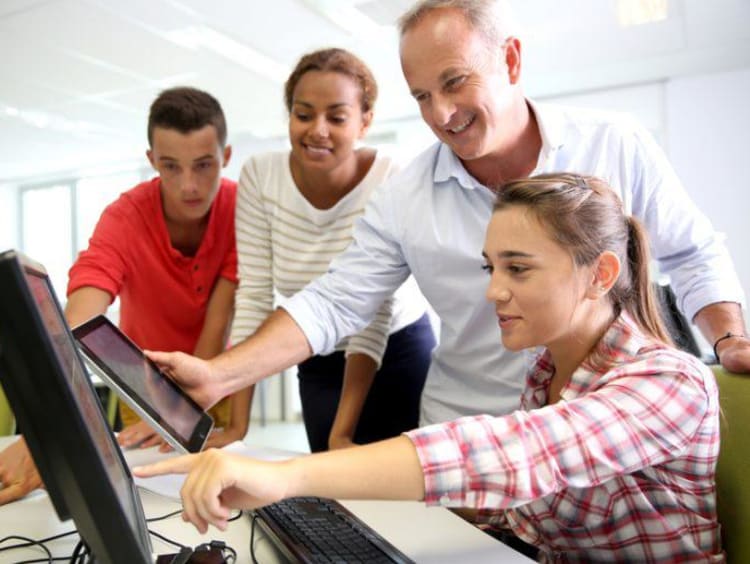 girl pointing to a computer and three other people watching