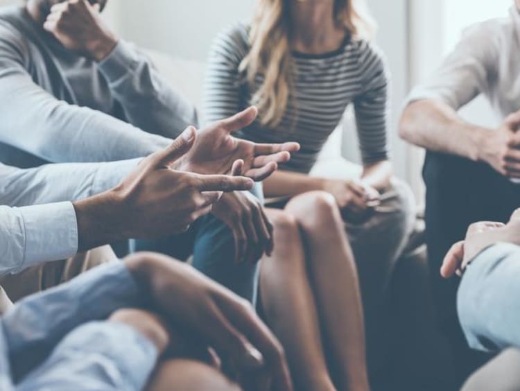 Group of people sit close together in a circle and listen to a speaker