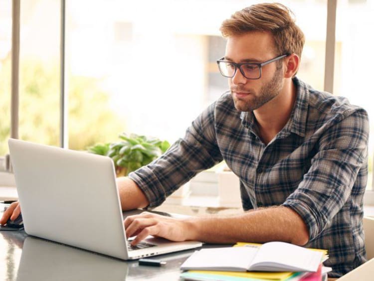 Man in plaid shirt researches online degree programs on laptop