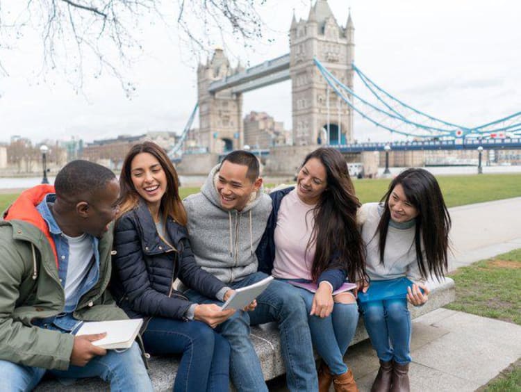 group of students sitting on bench in front of Tower Bridge in London