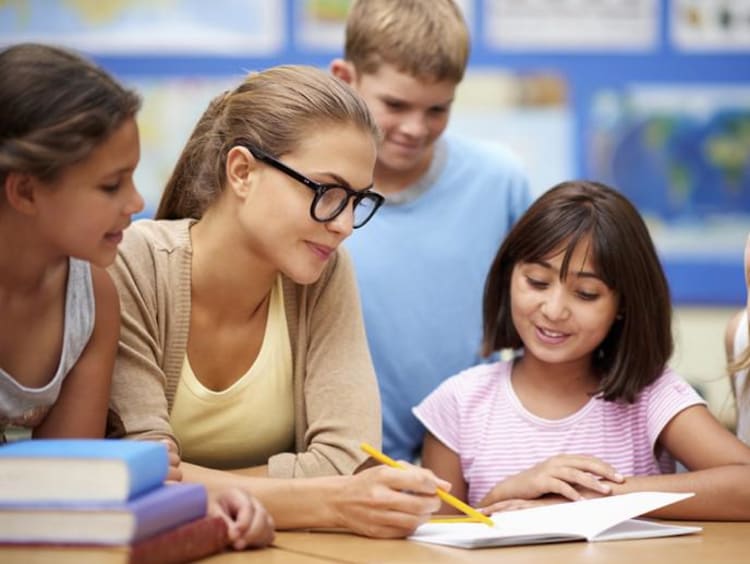 Teacher points to a word in book with students huddled around her