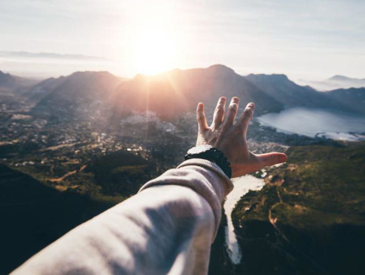 arm reaching towards mountains