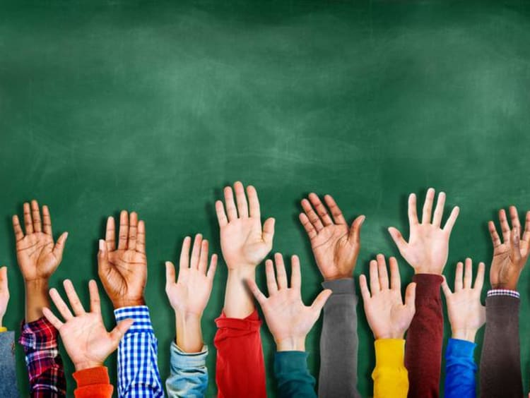 group of children raising hands in front of chalkboard