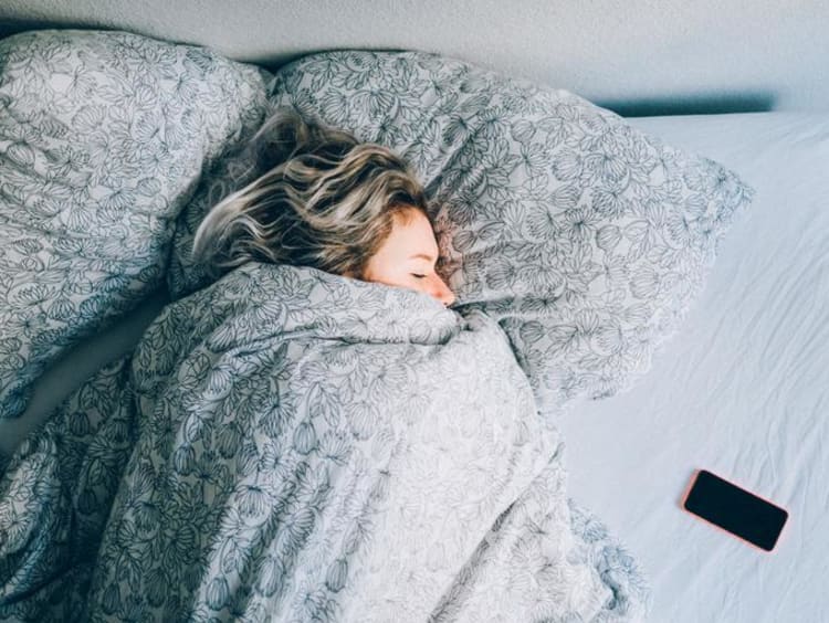 Woman sleeping in bed with her phone beside her