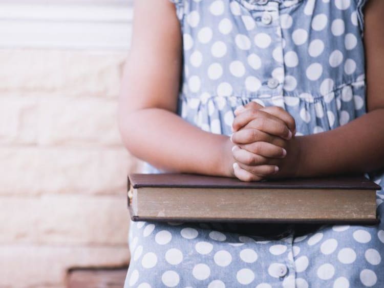 persons hands folded on bible