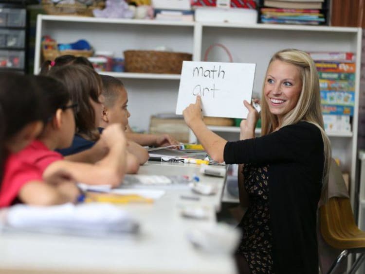 teacher holding whiteboard and teaching students