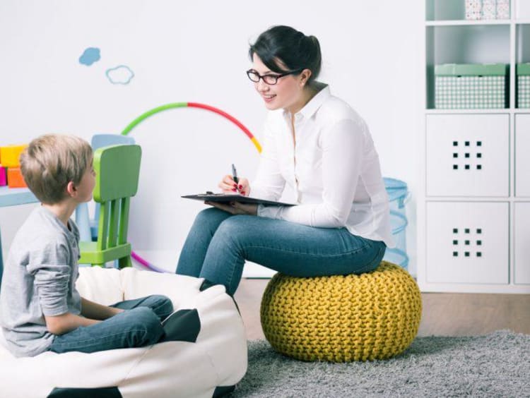 A family therapist sits in playroom and asks a little boy questions