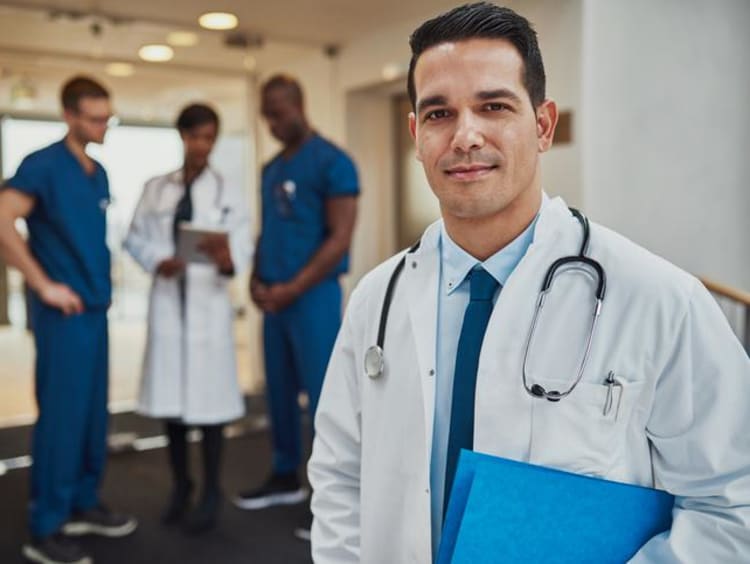 a male doctor in a white coat standing in front of other doctors discussing a case